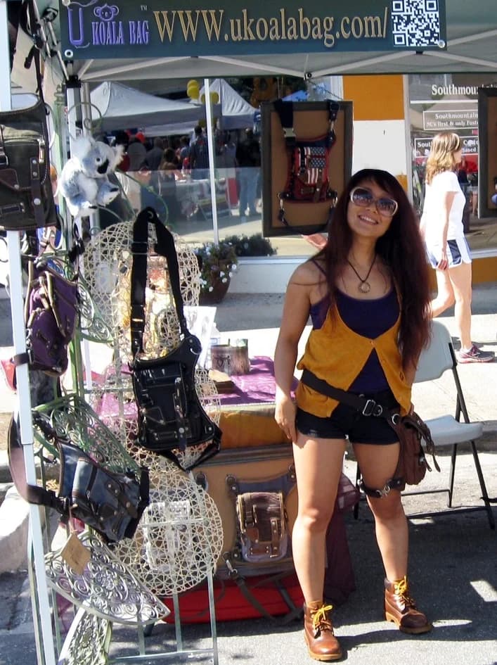 Mayan smiling beside hanging bag displays at one of Ukoala's first outdoor festival booths