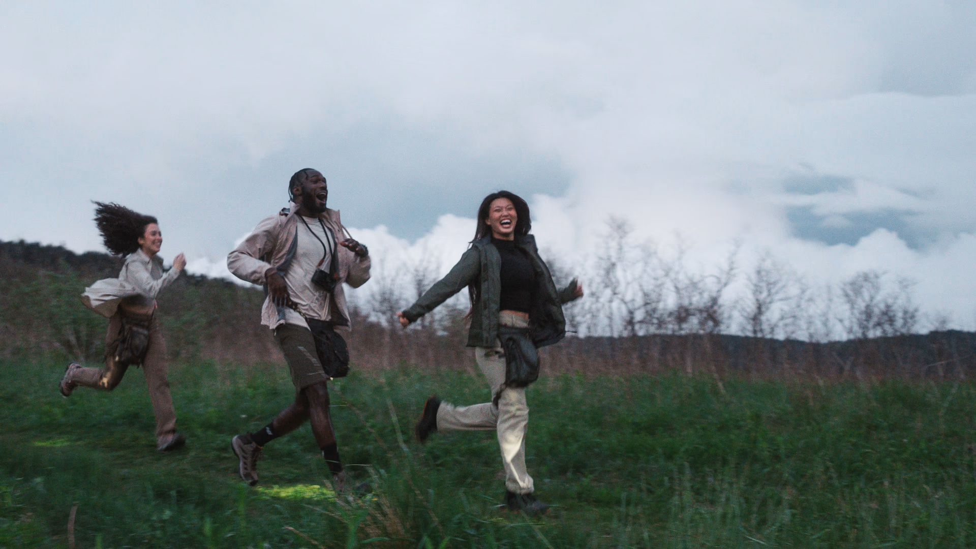 Three friends wearing Ukoala bags while running together through an open field