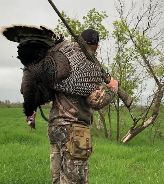 Hunter in camo carrying a wild turkey over the shoulder with a camo Ukoala bag on the thigh