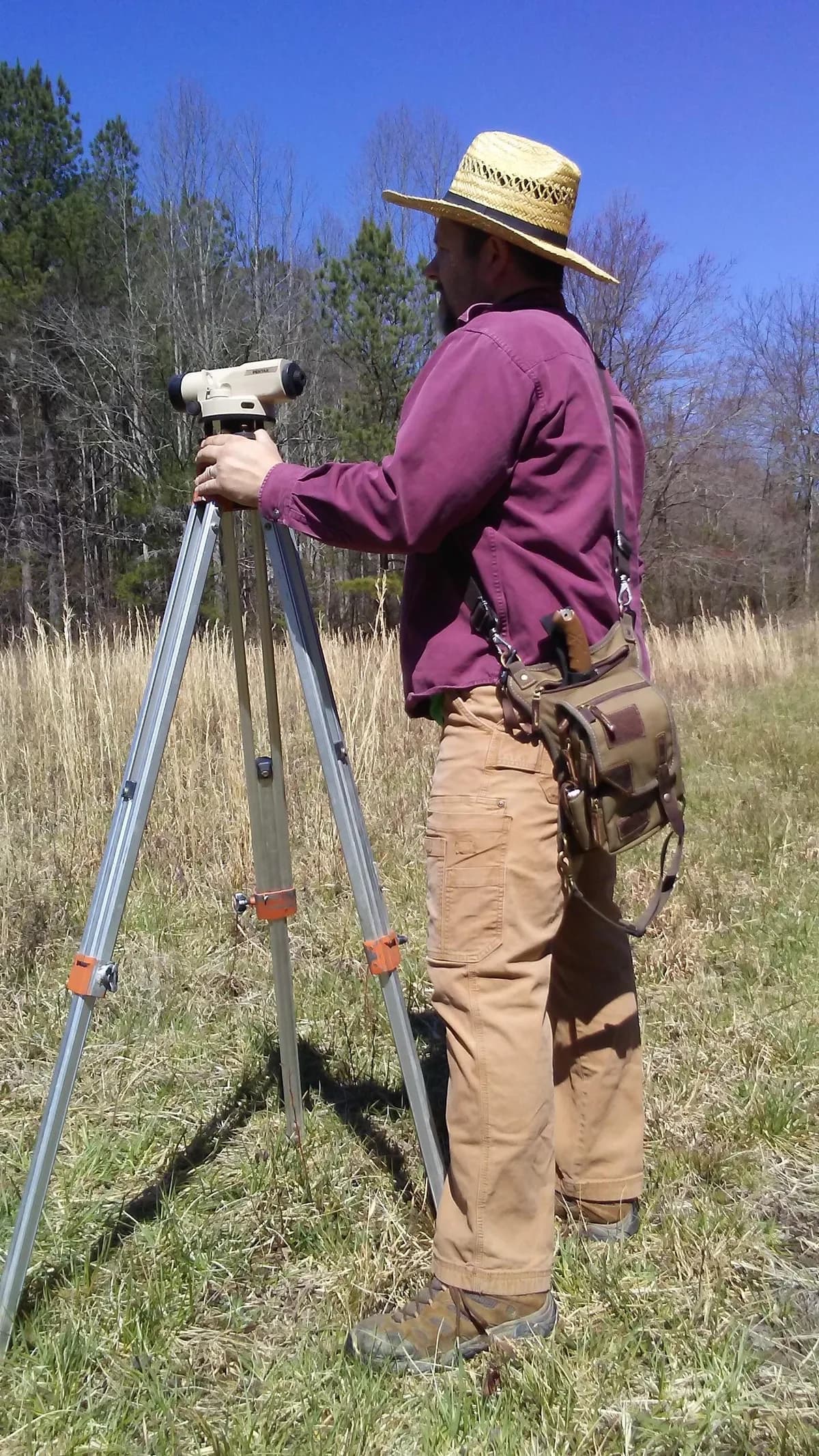 Land surveyor working at a tripod level in a field with a leather Ukoala bag at the hip