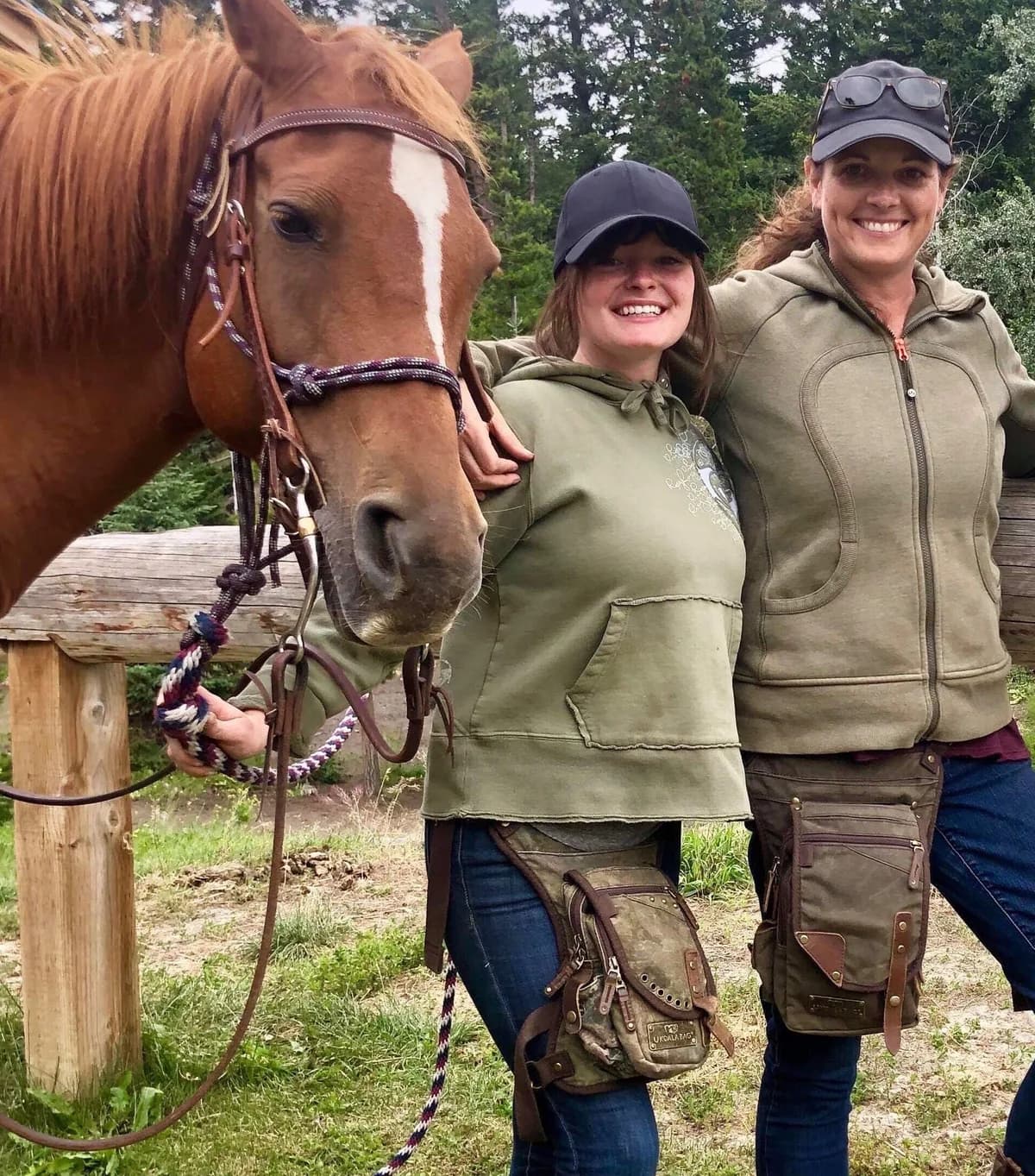 Two riders wearing matching camo Ukoala bags standing beside their horse